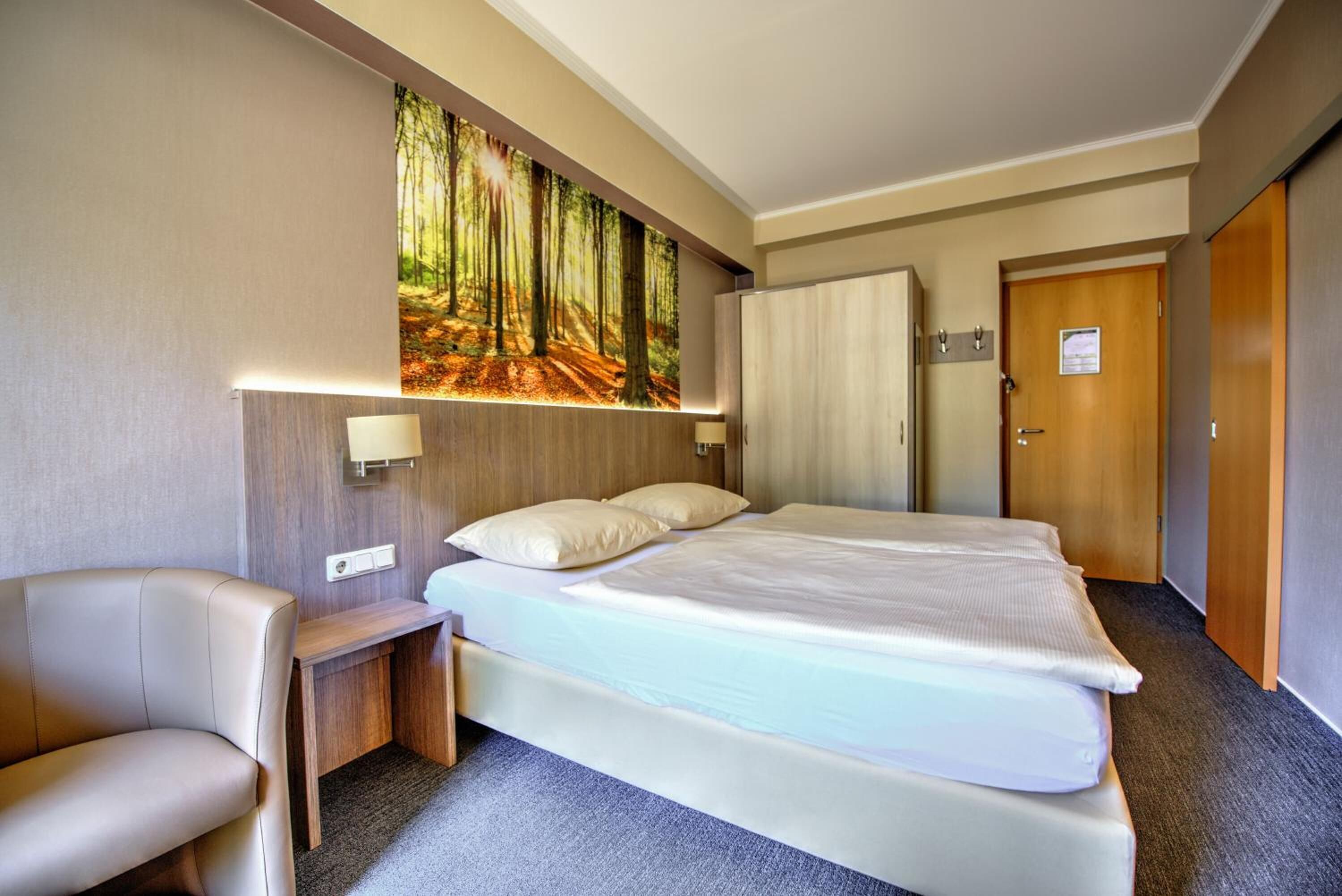A hotel room with a large bed, a chair, a desk, and a wall-mounted TV.