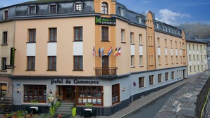 A hotel with a sign reading "Hotel du Commerce" and multiple flags.