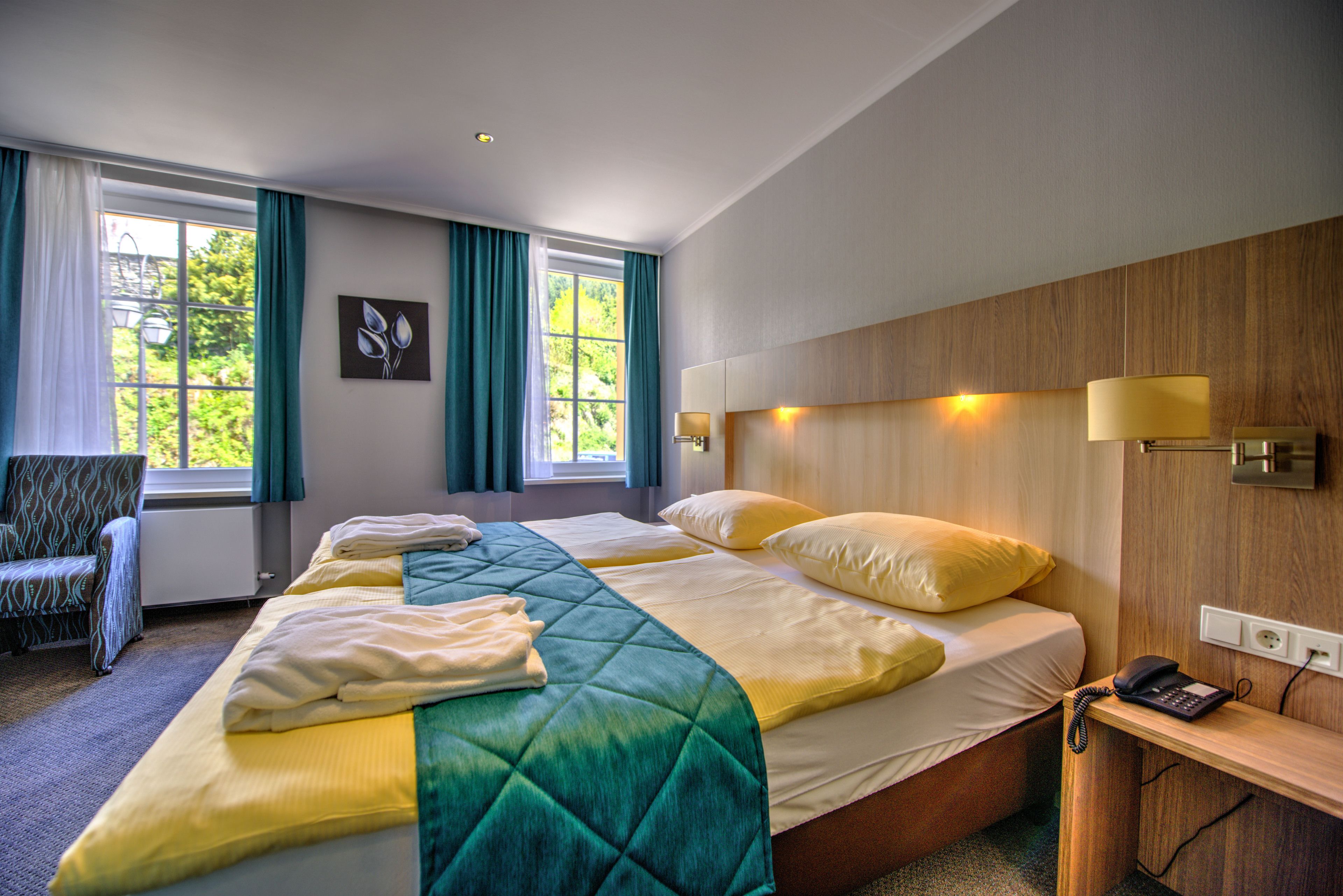 Ein Hotelzimmer mit einem großen Bett, einem Sessel, einem Schreibtisch mit Telefon und einem fenster mit Vorhängen.