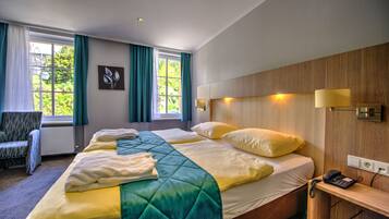 Ein Hotelzimmer mit einem großen Bett, einem Sessel, einem Schreibtisch mit Telefon und einem fenster mit Vorhängen.