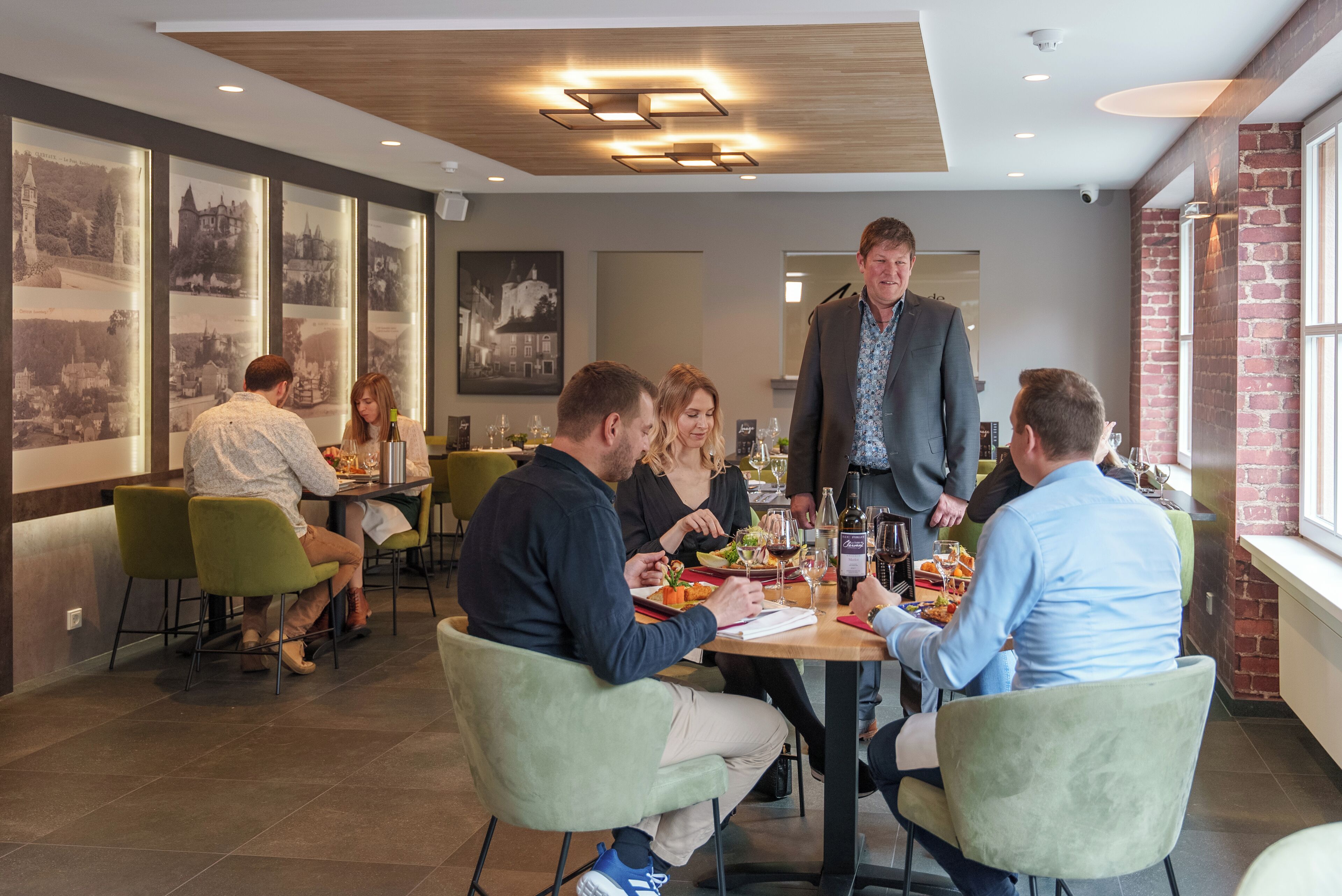 A restaurant with a modern interior, featuring green chairs, a wooden table, and framed pictures on the wall.
