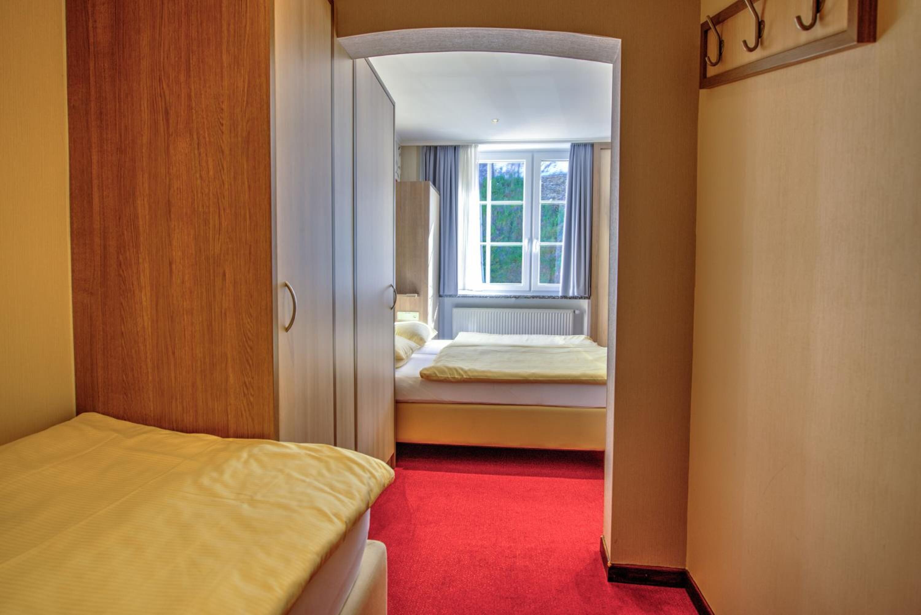 Ein enger Flur führt zu einem Schlafzimmer mit einem Bett und einem Fenster.