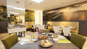 A modern dining area with a large table set for breakfast, including bread, pastries, and beverages.