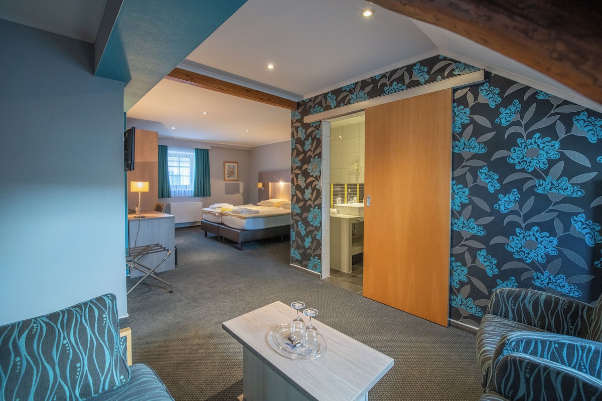 A hotel room with a bed, a desk, a chair, and a table with a tray.