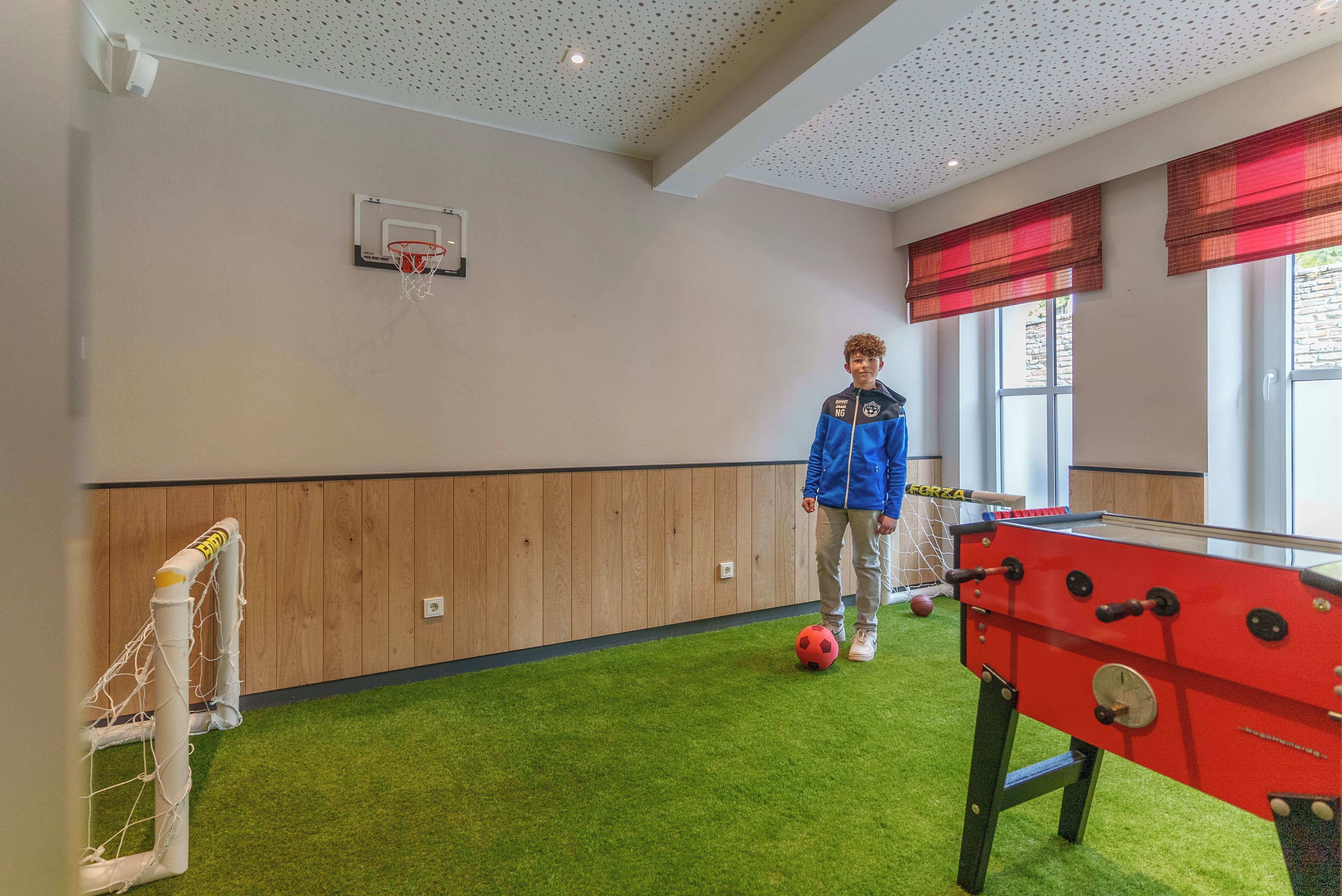 Um quarto com mesa de pebolim, cesta de basquete e janela com cortinas vermelhas.