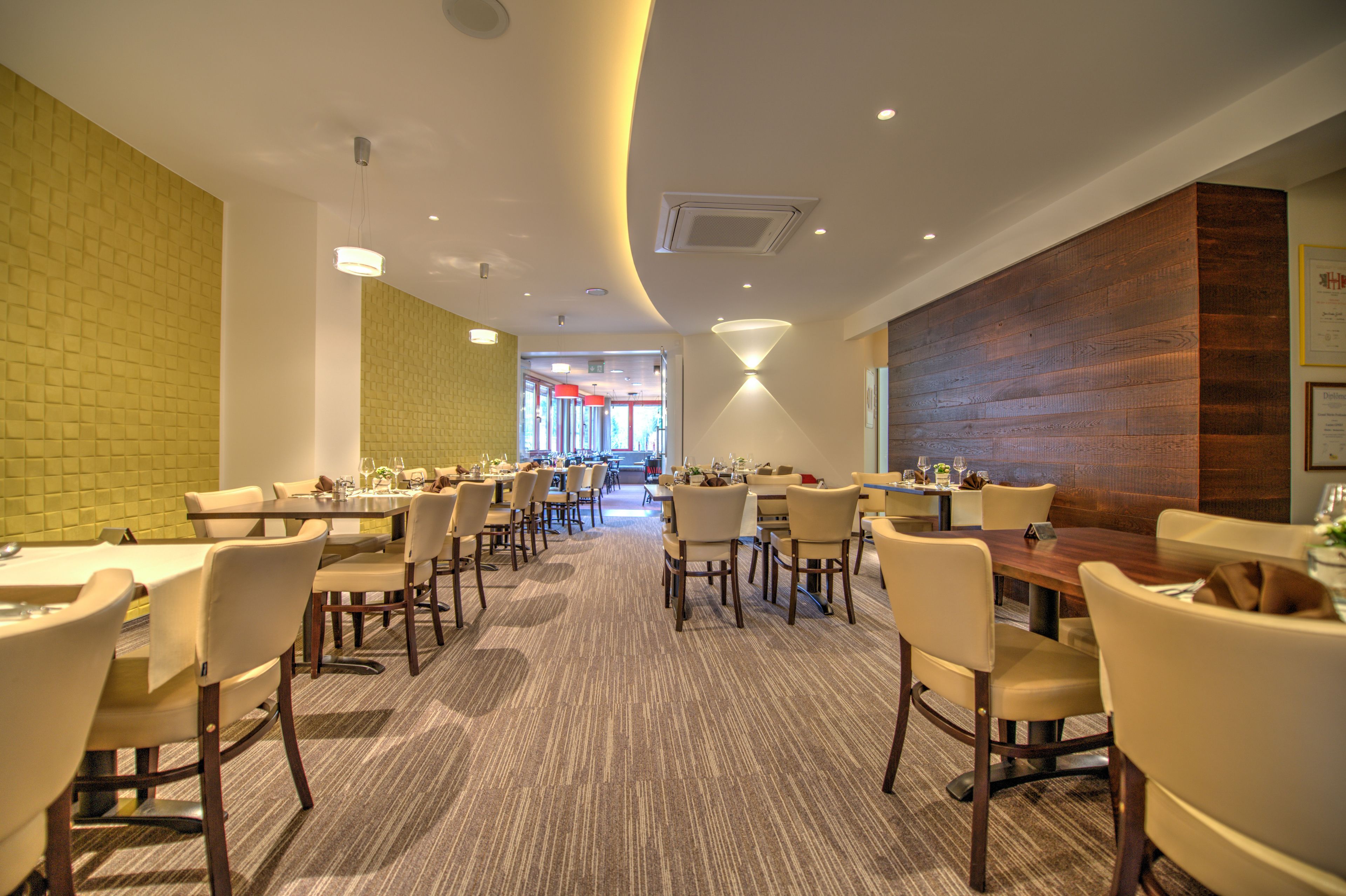 A spacious dining area with multiple tables and chairs, a carpeted floor, and a brick wall on one side.