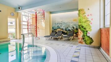 An indoor swimming pool with a spiral staircase, lounge chairs, and a mural of waves.