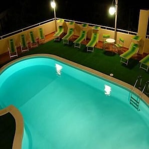 A swimming pool with a slide, surrounded by lounge chairs and a small table.