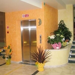 An elevator with a metallic finish, a wall-mounted sign, and a potted plant with white flowers.