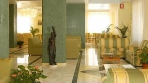 Un vestíbulo con suelo de mármol, columnas verdes, una estatua y sofás a rayas.