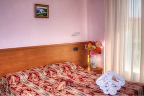 A hotel room with a wooden headboard, a patterned bedspread, a vase with flowers, and a window with curtains. - Hotel Ave (Chianciano Terme)