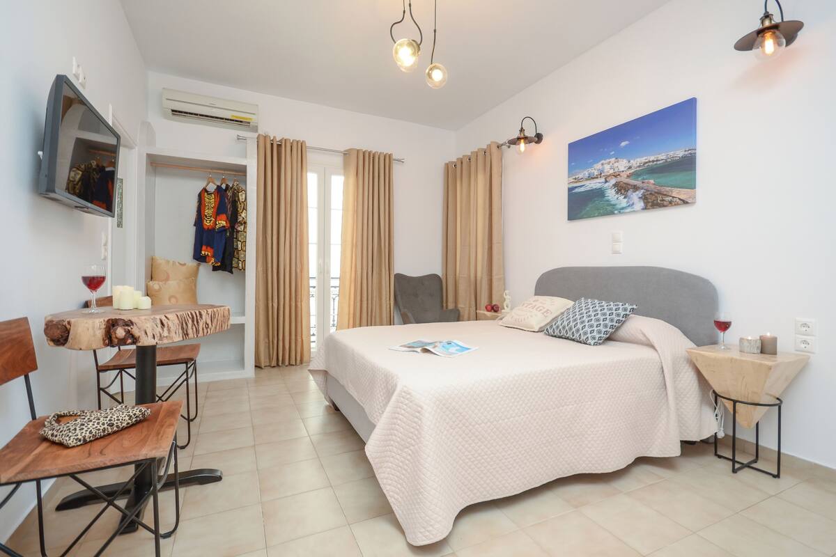 A bedroom with a bed, a desk, a chair, a TV, and a painting on the wall.