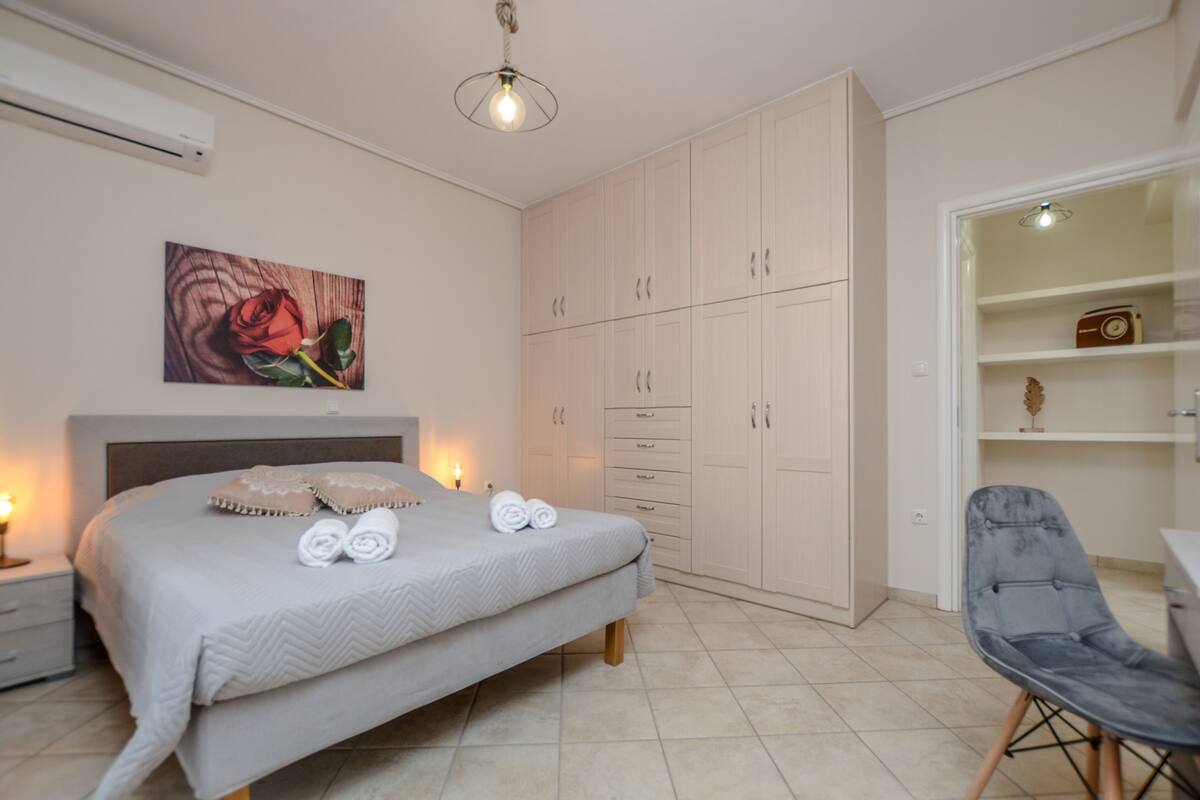 A bedroom with a bed, bedside lamps, a wardrobe, a chair, and a painting on the wall.