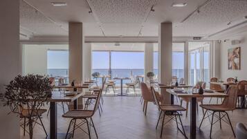 A spacious dining area with tables and chairs, large windows offering a view of the sea, and a sign indicating the exit.