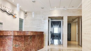 Zona de recepción de hotel con un mostrador de mármol, un cartel en la pared y un pasillo que conduce a otras habitaciones.