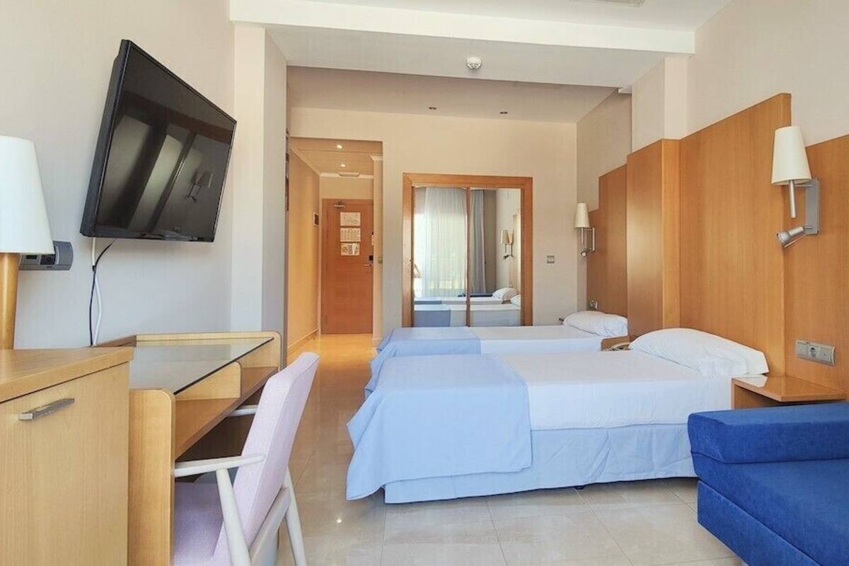 A hotel room with a desk, two beds, a TV, and a mirror.