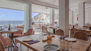 Un restaurante con mesas y sillas, amplias ventanas y vista al mar.