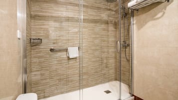 Une cabine de douche fermée par des parois en verre, avec un mur carrelé, une serviette blanche et un porte-serviettes en métal.
