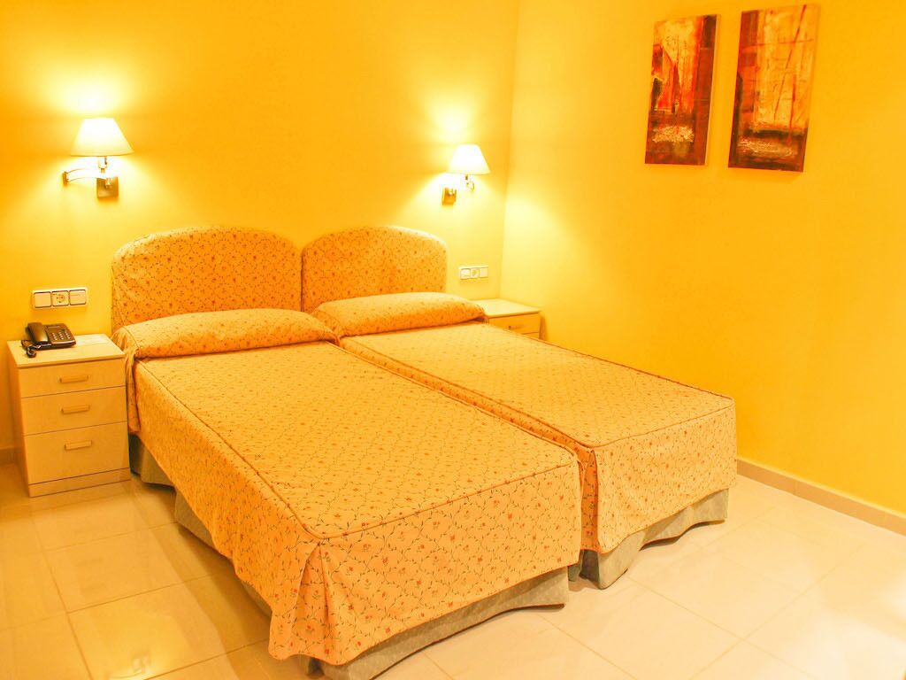 A double bed with a floral bedspread, two bedside lamps, a nightstand, and a telephone.