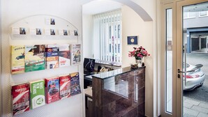 A hotel reception area with a marble counter, a computer, and various promotional materials on the walls. - Hotel DomBlick (Cologne)