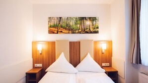 A hotel room with a large bed, two bedside tables, and a wall-mounted painting of a forest scene. - Hotel DomBlick (Cologne)