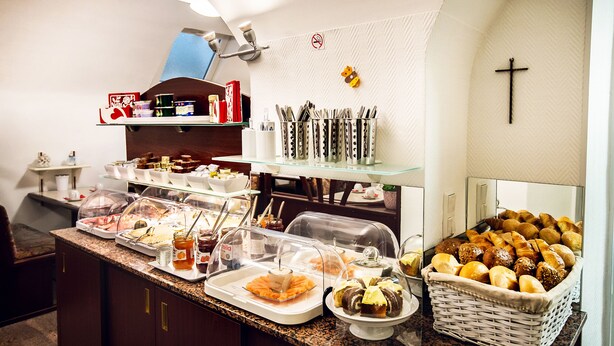 A buffet with various food items, including pastries and bread, arranged on a counter with glass display cases. - Hotel DomBlick (Cologne)