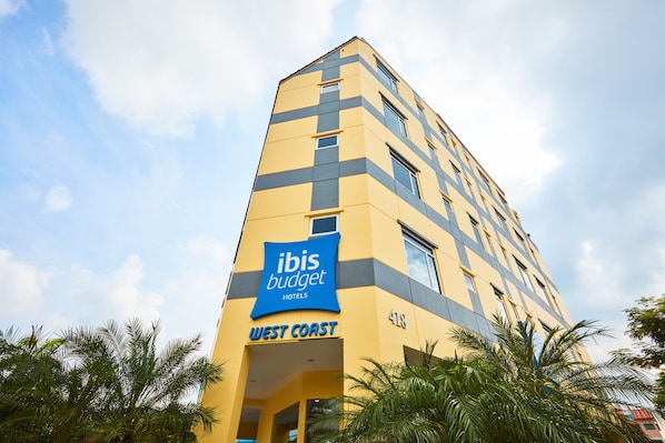Un grand immeuble d’hôtel avec une enseigne bleue sur laquelle on peut lire « Ibis Budget West Coast ».