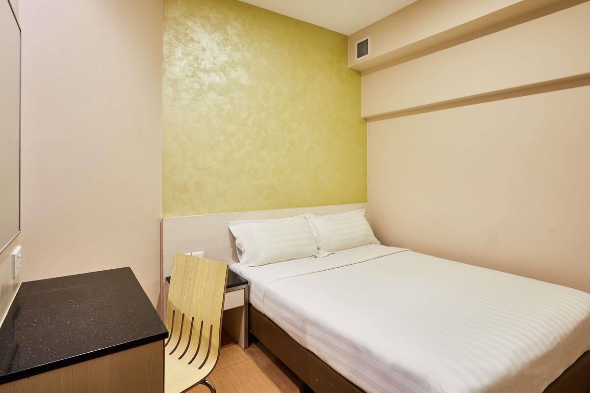 A small, neatly arranged room with a bed, a desk, and a chair.
