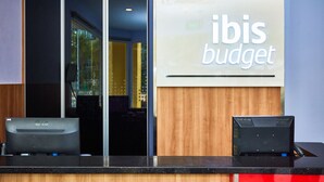 A reception desk with a sign reading "ibis budget" and two computers on the counter. - ibis budget Singapore West Coast (Singapore)