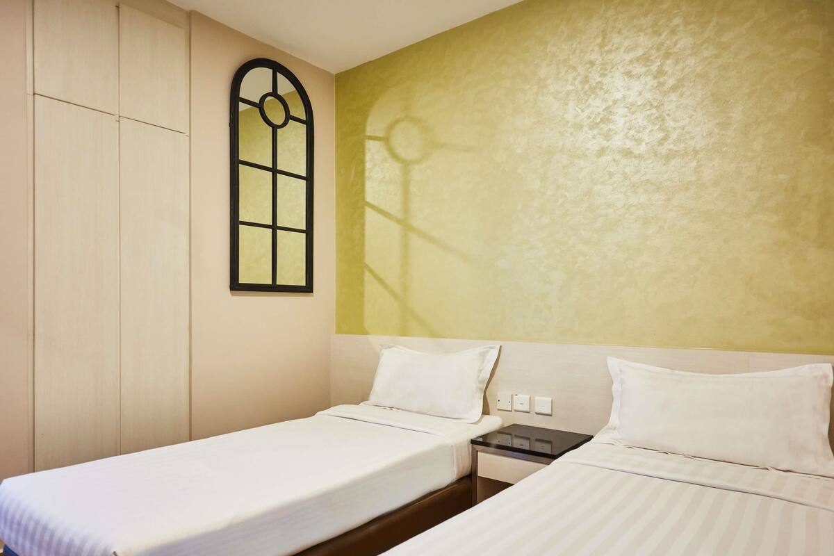 A hotel room with two single beds, a small bedside table, a wall-mounted window, and a textured wall.