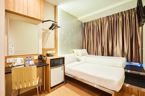 A hotel room with a bed, a desk with a telephone, a small refrigerator, and a mirror. - ibis budget Singapore West Coast (Singapore)