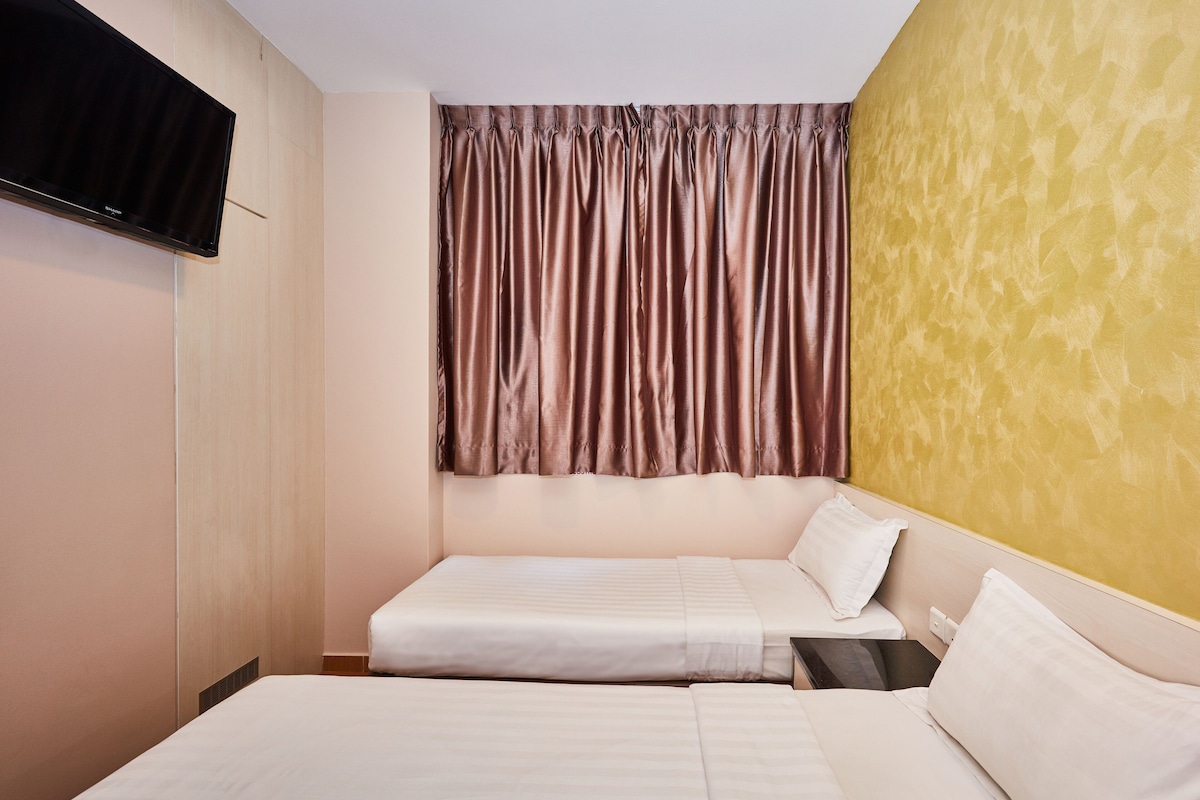 Ein Hotelzimmer mit zwei Betten, einem an der Wand befestigten Flachbildfernseher und einem Vorhang, der das Fenster verdeckt.