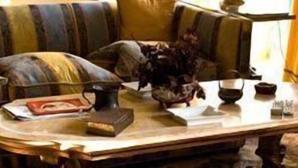 Una habitación con un sofá, una mesa con un libro, un jarrón y una mesita con una vela y un vaso.