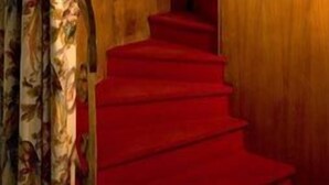 Una escalera con alfombra roja que lleva a una puerta de madera.