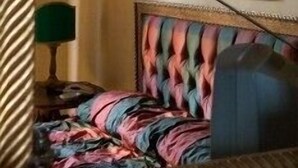 Habitación de hotel con cama y un cabecero de diseño colorido, un cuadro en la pared y una lámpara verde sobre una mesita de noche.