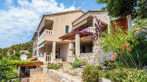 A two-story stone house with a balcony, surrounded by lush greenery and a stone wall. - Villa Perka (Hvar)