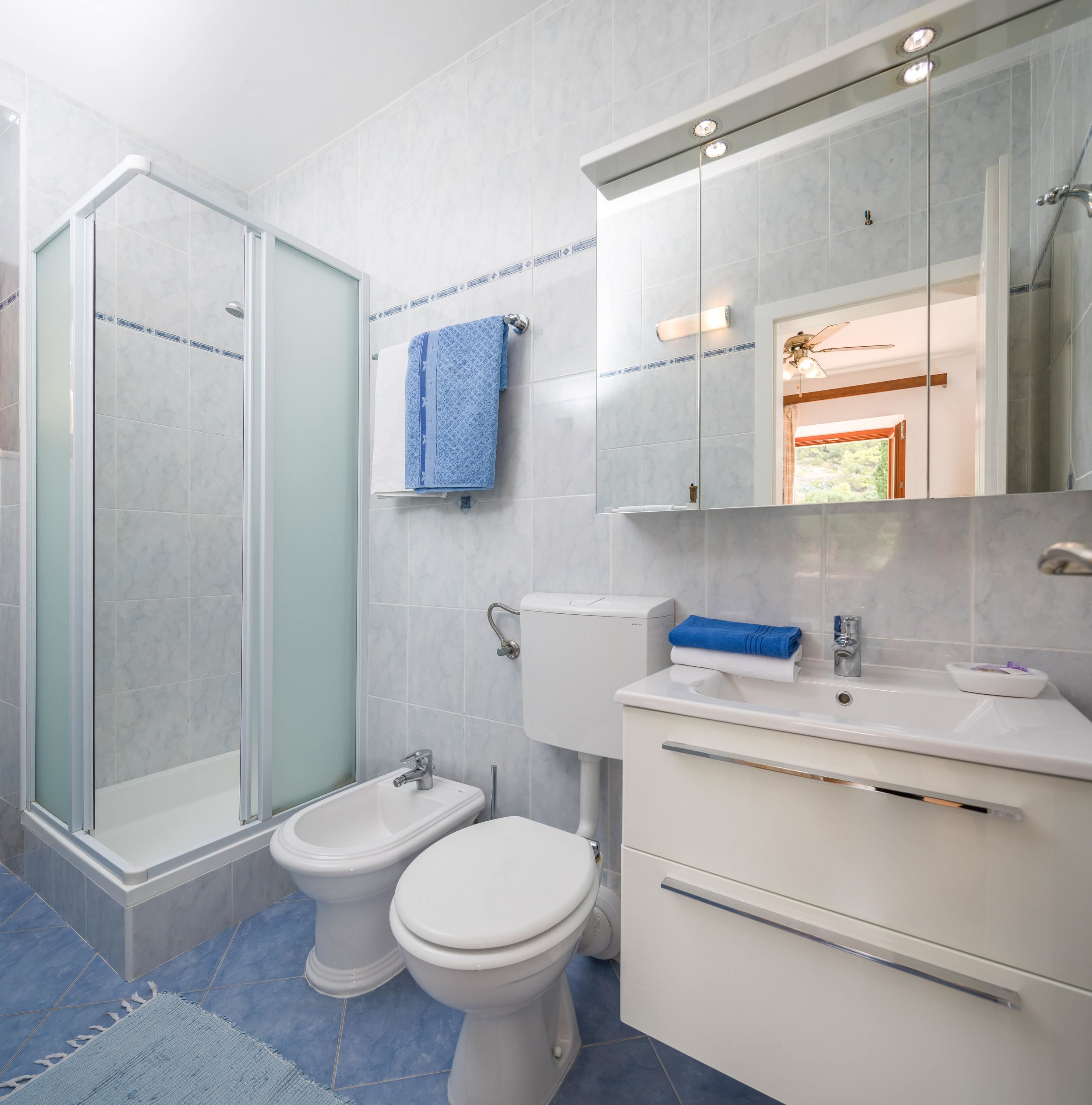 A modern bathroom with a glass shower enclosure, two toilets, a sink with a mirror, and a blue towel on the wall.