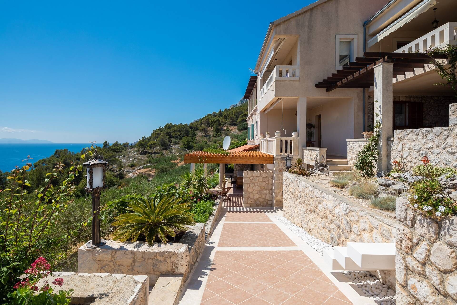 A two-story house with a stone facade, a wooden pergola, and a view of the sea.