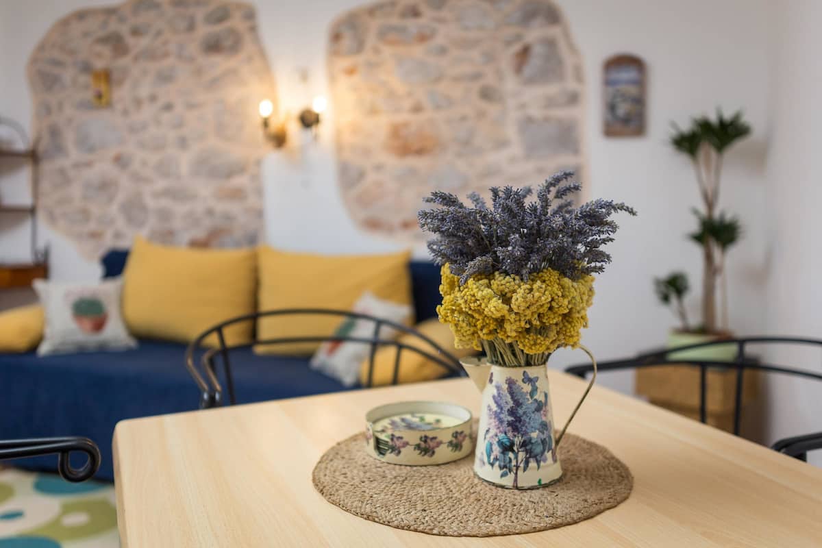 A room with a wooden table, a vase with flowers, a small decorative bowl, and a stone wall in the background.