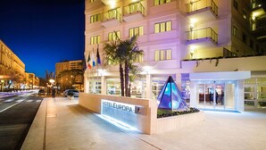 A hotel entrance with a sign reading "HOTEL EUROPA", a modern building with balconies, and a well-lit street in the background.