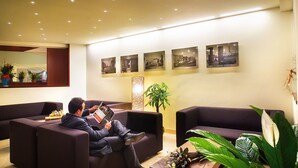 A modern lobby with dark sofas, a large mirror, and wall-mounted photographs.