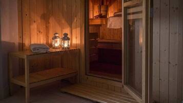 Ein Holz-Saunaraum mit einer Sitzbank, einem Ablagefach mit Handtüchern und zwei beleuchteten Laternen.