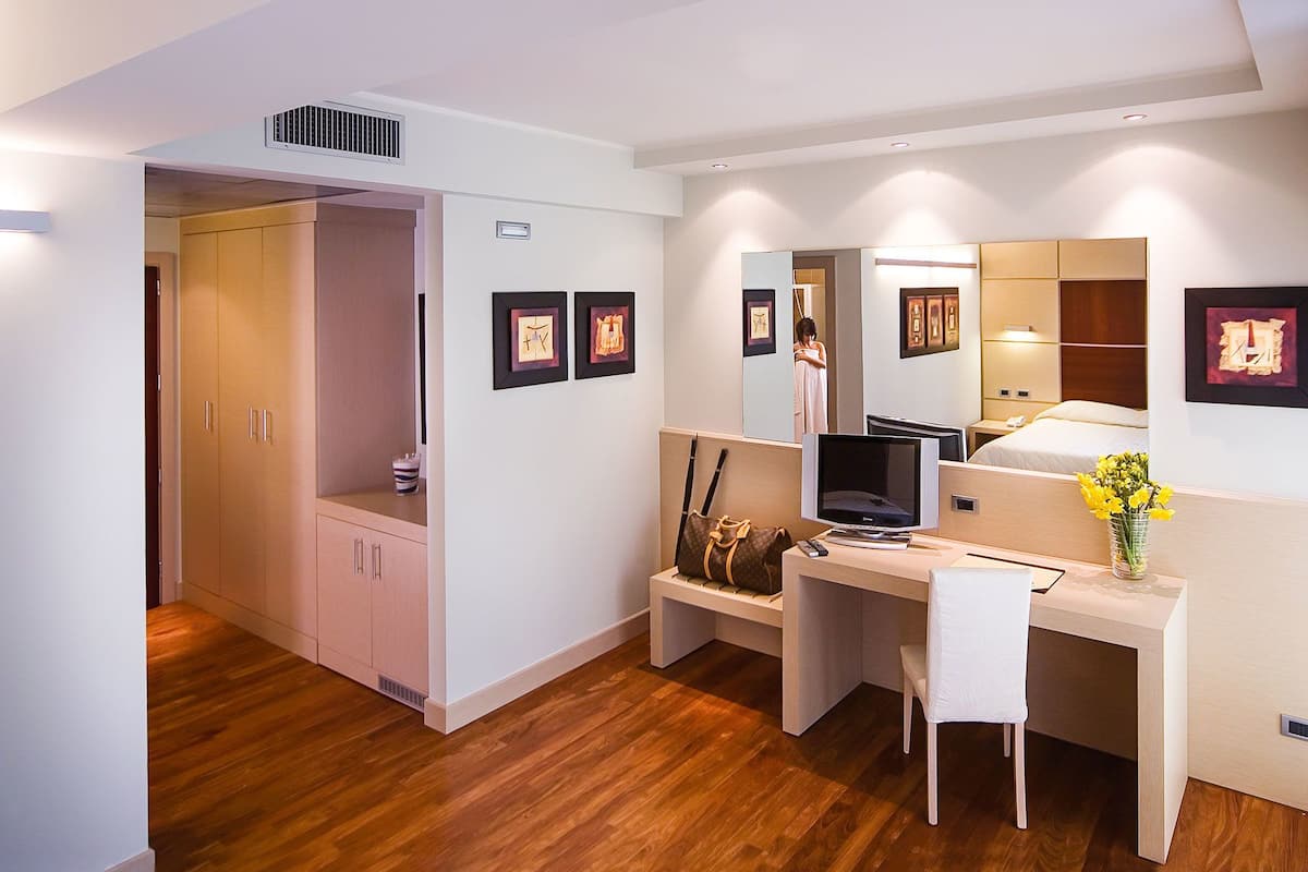 Ein Hotelzimmer mit Holzboden, Schreibtisch mit Stuhl, Bett, Kleiderschrank und Spiegel.