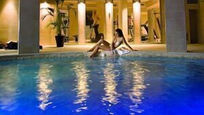 An indoor swimming pool with a modern design, featuring a skylight and a seating area with people around.