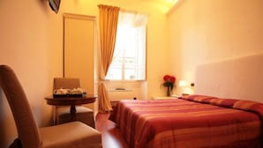 Una habitación de hotel con una cama, una silla, una mesita con una lámpara y una ventana con cortinas.