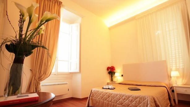Una habitación de hotel con cama, mesita de noche, lámpara y un jarrón con flores.