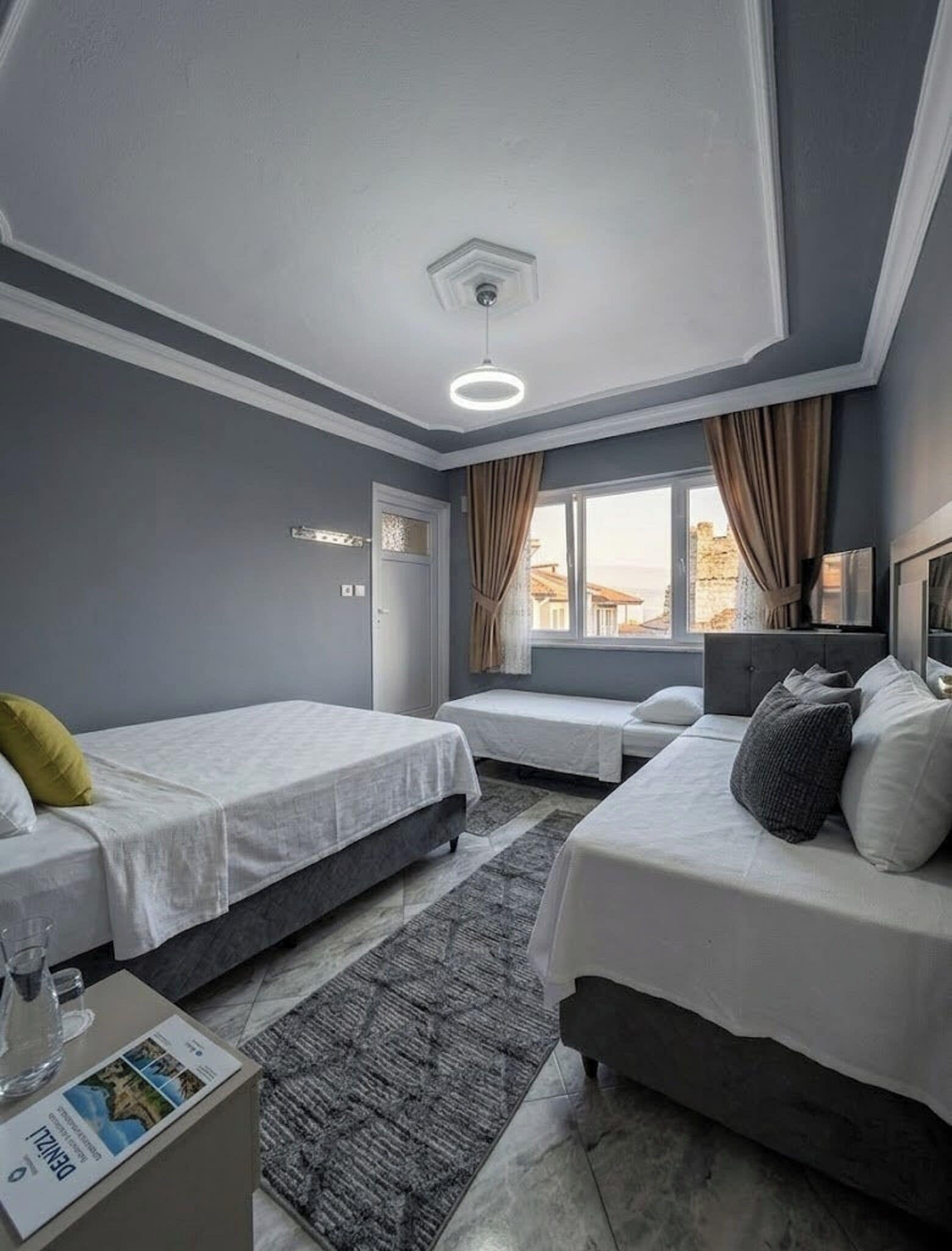 Een hotelkamer met twee bedden, een raam met gordijnen, een plafondlamp en uitzicht op gebouwen.