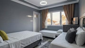 Habitación de hotel con dos camas, una ventana con cortinas, una lámpara en el techo y vistas a edificios.