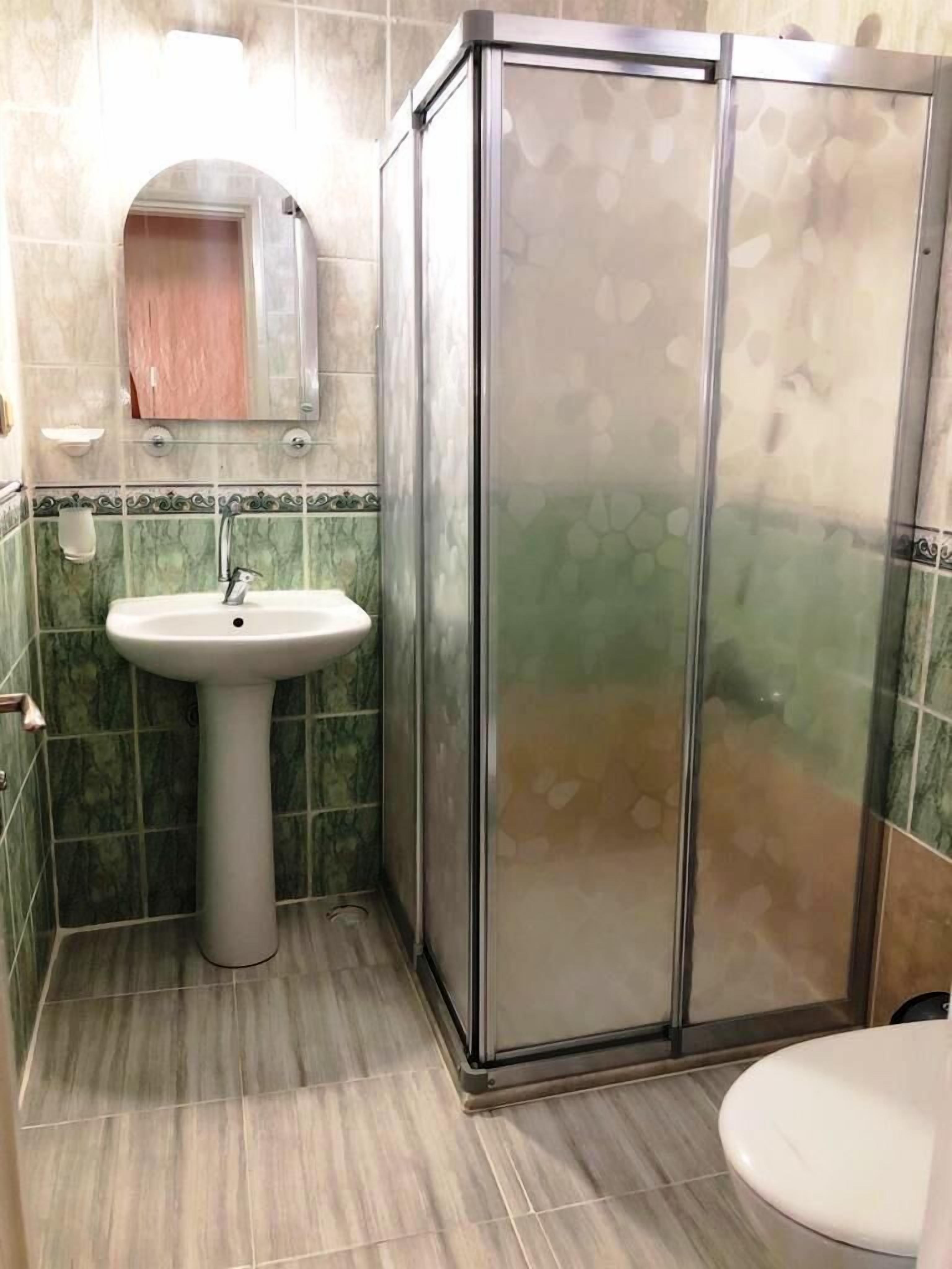 A bathroom with a pedestal sink, a glass shower enclosure, and a toilet.