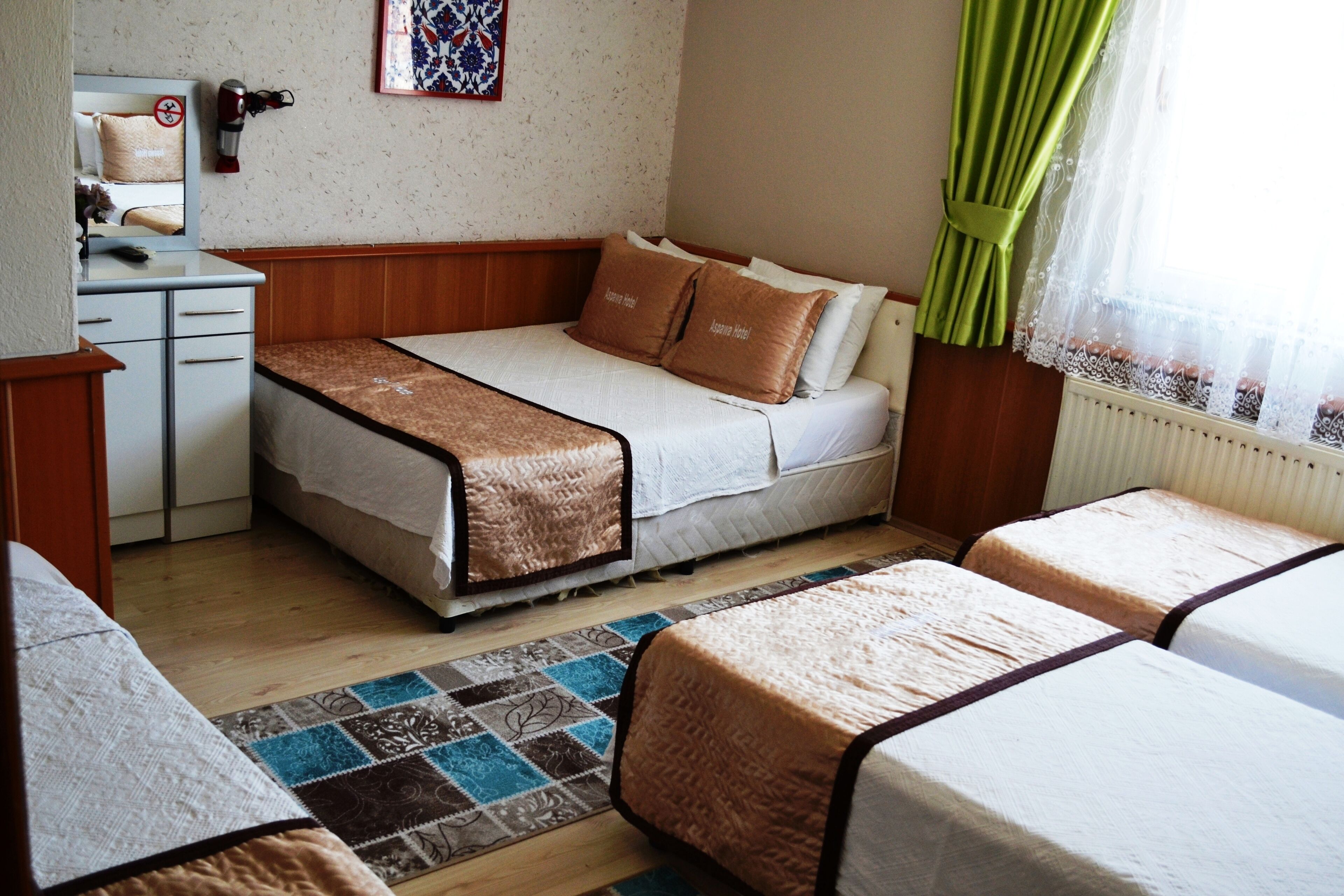 A hotel room with a bed, a desk, a mirror, and a window with curtains.